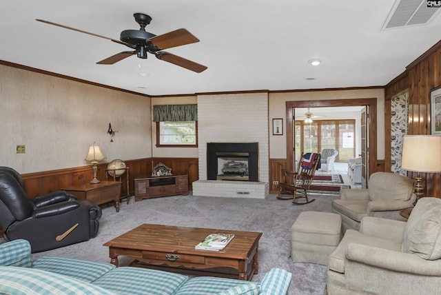 carpeted living room featuring a fireplace, ornamental molding, ceiling fan, and wood walls