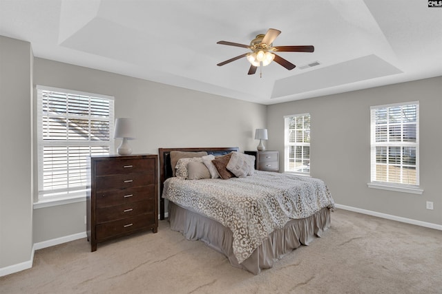 bedroom with multiple windows, light carpet, a raised ceiling, and ceiling fan