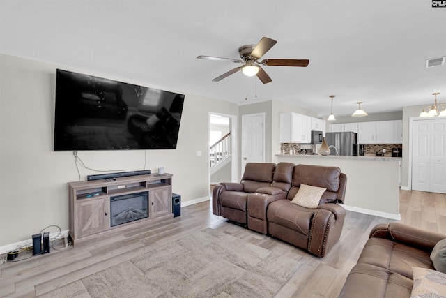 living room featuring ceiling fan with notable chandelier and light hardwood / wood-style flooring