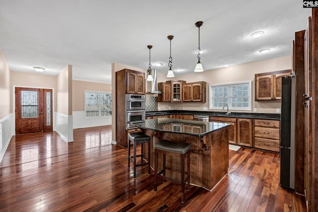 kitchen featuring dark wood-type flooring, stainless steel appliances, a center island, and wall chimney exhaust hood