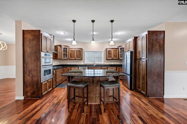 kitchen with a kitchen island, appliances with stainless steel finishes, decorative light fixtures, sink, and dark hardwood / wood-style flooring