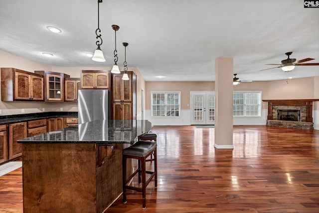 kitchen featuring a fireplace, stainless steel refrigerator, a breakfast bar area, hanging light fixtures, and dark wood-type flooring