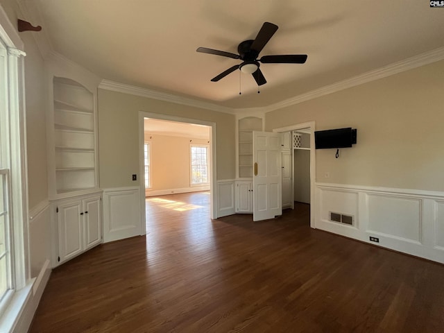 interior space with built in shelves, dark wood-type flooring, ornamental molding, and ceiling fan