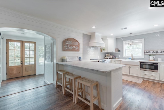 kitchen with premium range hood, sink, a breakfast bar area, white cabinetry, and light stone countertops