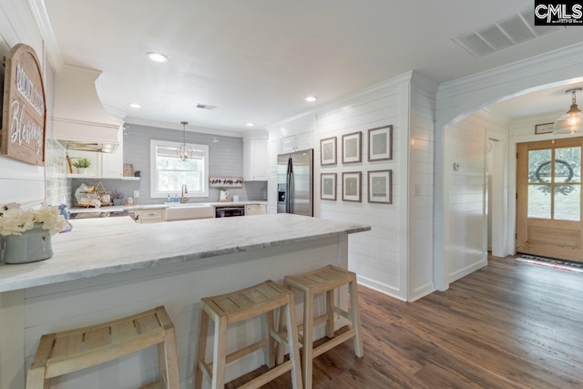 kitchen featuring white cabinetry, hanging light fixtures, stainless steel refrigerator with ice dispenser, a kitchen bar, and kitchen peninsula