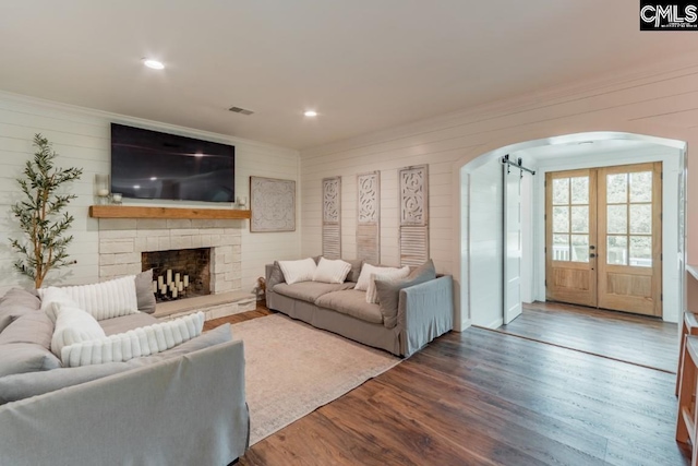 living room featuring hardwood / wood-style floors, a fireplace, wood walls, crown molding, and french doors