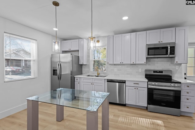 kitchen featuring appliances with stainless steel finishes, white cabinetry, sink, decorative backsplash, and hanging light fixtures