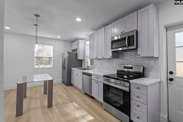 kitchen featuring pendant lighting, sink, light hardwood / wood-style flooring, appliances with stainless steel finishes, and tasteful backsplash