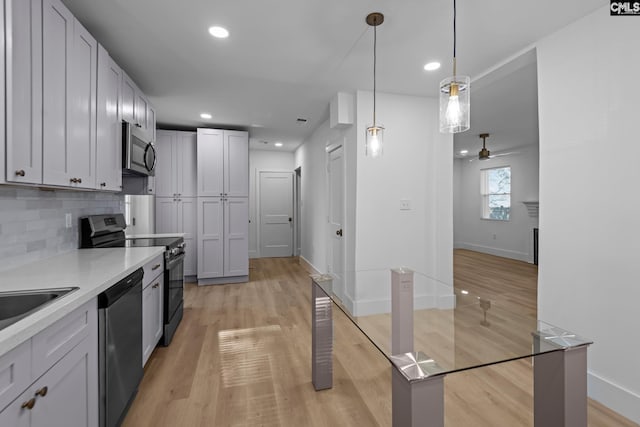 kitchen featuring appliances with stainless steel finishes, white cabinetry, hanging light fixtures, decorative backsplash, and light wood-type flooring