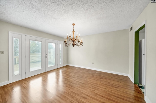 unfurnished dining area featuring hardwood / wood-style flooring, a notable chandelier, french doors, and a textured ceiling