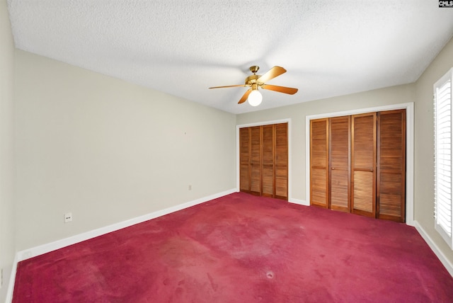 unfurnished bedroom with ceiling fan, carpet floors, a textured ceiling, and two closets