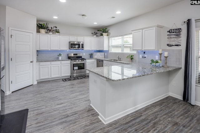 kitchen with sink, white cabinetry, appliances with stainless steel finishes, kitchen peninsula, and hardwood / wood-style floors