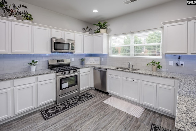 kitchen featuring sink, light hardwood / wood-style flooring, white cabinetry, backsplash, and stainless steel appliances