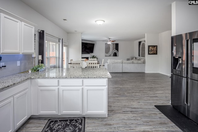 kitchen featuring black fridge with ice dispenser, white cabinetry, light stone counters, kitchen peninsula, and ceiling fan