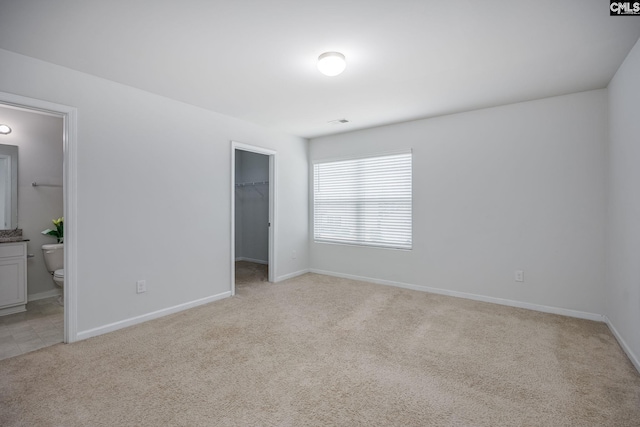 unfurnished bedroom with a walk in closet, ensuite bathroom, a closet, and light carpet