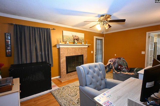 living room featuring crown molding, ceiling fan, a tiled fireplace, and light hardwood / wood-style flooring