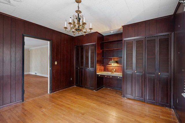 interior space featuring two closets, a notable chandelier, light hardwood / wood-style floors, and wood walls