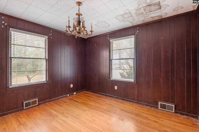 spare room with a wealth of natural light, light hardwood / wood-style floors, wooden walls, and a chandelier