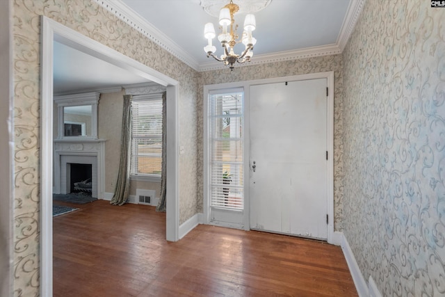 foyer entrance featuring ornamental molding, wood-type flooring, a large fireplace, and an inviting chandelier