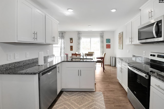 kitchen with sink, white cabinetry, dark stone countertops, stainless steel appliances, and kitchen peninsula