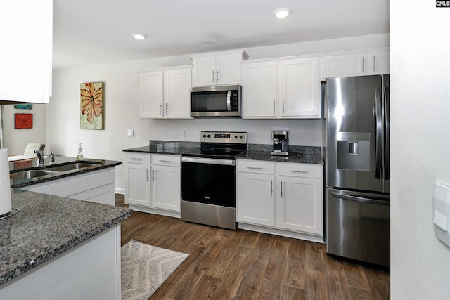 kitchen with sink, white cabinetry, appliances with stainless steel finishes, dark hardwood / wood-style floors, and dark stone counters