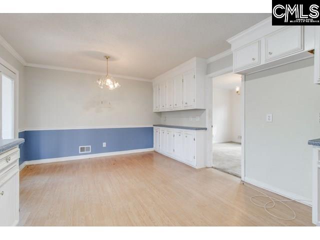 kitchen featuring white cabinetry, ornamental molding, light hardwood / wood-style floors, and a chandelier