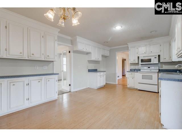 kitchen with crown molding, a notable chandelier, white appliances, light hardwood / wood-style floors, and white cabinets