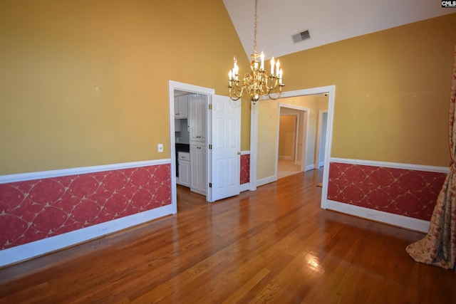 unfurnished dining area featuring an inviting chandelier, wood-type flooring, and high vaulted ceiling