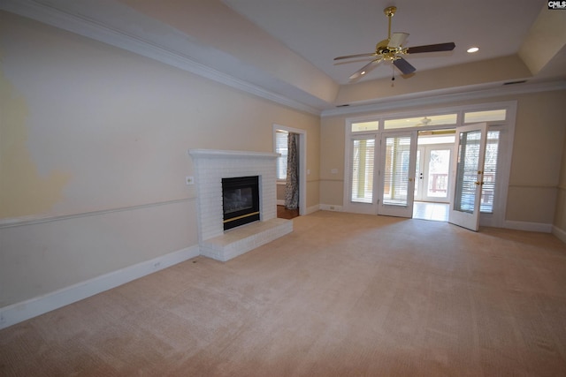 unfurnished living room featuring light carpet, ornamental molding, a tray ceiling, ceiling fan, and a fireplace