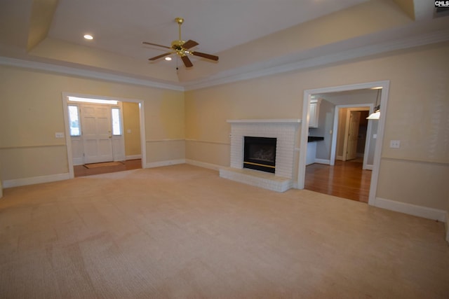 unfurnished living room featuring carpet flooring, ornamental molding, a tray ceiling, and a brick fireplace