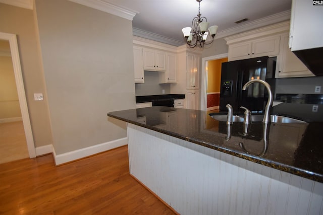 kitchen with black fridge with ice dispenser, crown molding, decorative light fixtures, dark stone countertops, and white cabinets