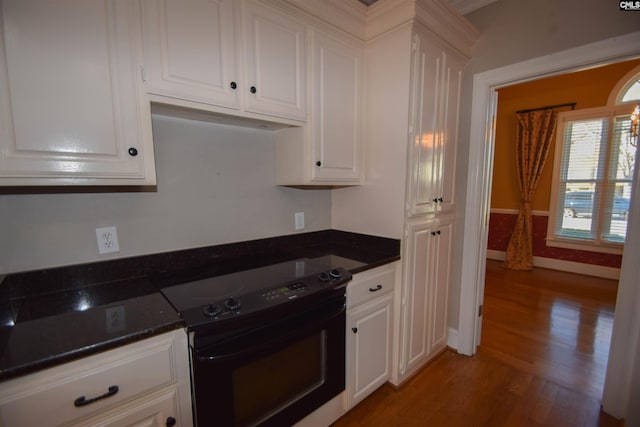 kitchen with hardwood / wood-style flooring, dark stone countertops, black range with electric stovetop, and white cabinets