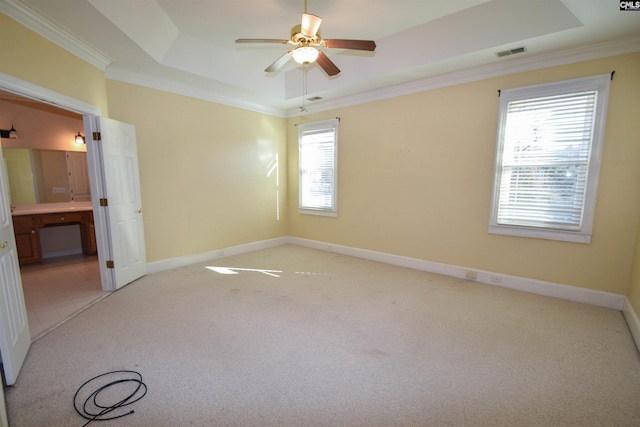 empty room with crown molding, a tray ceiling, light colored carpet, and ceiling fan