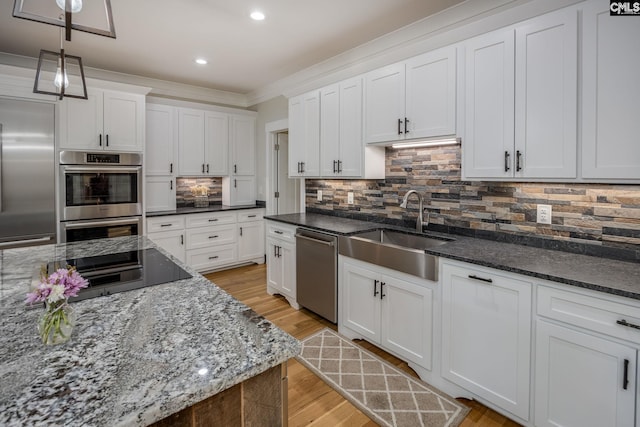 kitchen with a sink, white cabinets, appliances with stainless steel finishes, light wood-type flooring, and backsplash