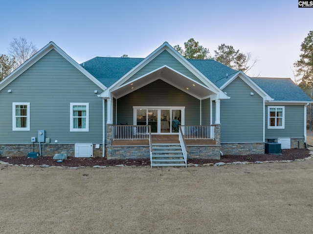 view of front facade featuring covered porch, roof with shingles, and central AC unit