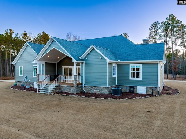 view of front of house with a shingled roof, central AC unit, a chimney, covered porch, and a front lawn