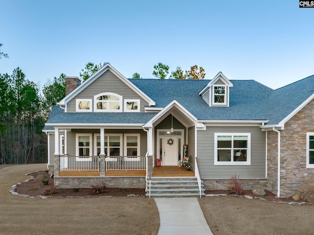 view of front of home featuring stone siding, covered porch, roof with shingles, and a chimney