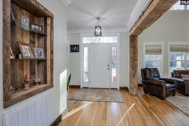 entryway with light wood-type flooring, ornamental molding, and plenty of natural light