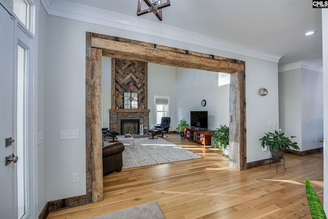 living room featuring light wood finished floors, a fireplace, baseboards, and crown molding