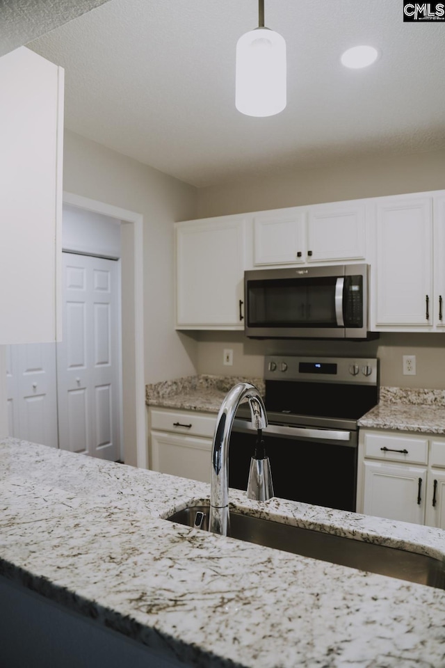 kitchen with appliances with stainless steel finishes, pendant lighting, white cabinets, and light stone counters