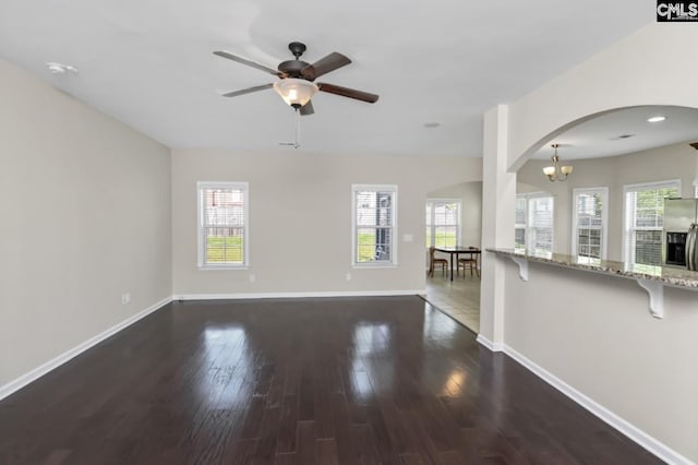 unfurnished living room with ceiling fan with notable chandelier, dark hardwood / wood-style floors, and a wealth of natural light