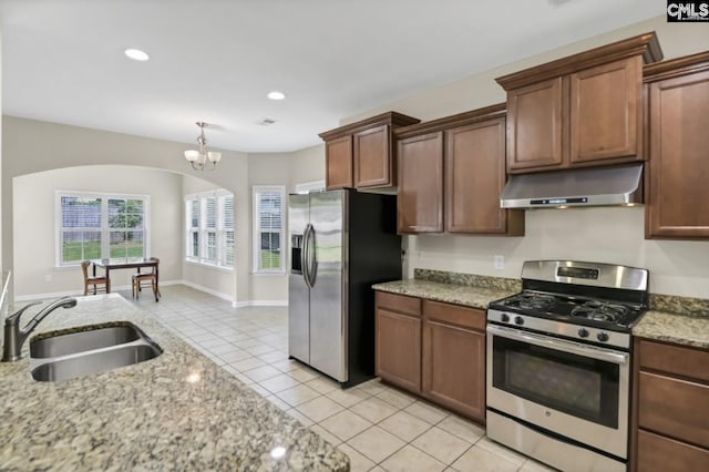 kitchen with light tile patterned flooring, sink, hanging light fixtures, light stone counters, and stainless steel appliances