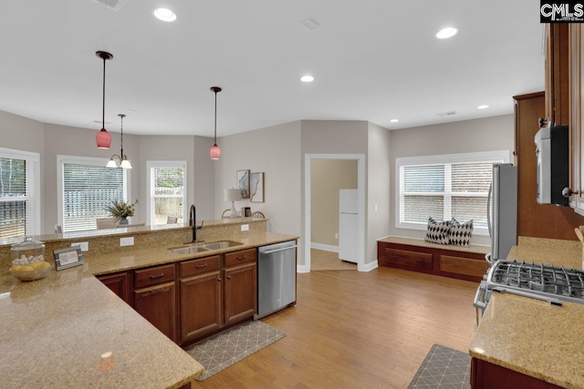 kitchen with light stone counters, sink, decorative light fixtures, and stainless steel appliances