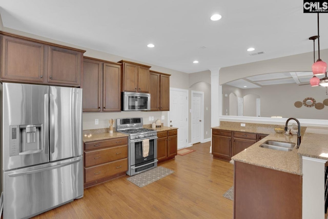 kitchen with sink, appliances with stainless steel finishes, hanging light fixtures, light stone counters, and light wood-type flooring