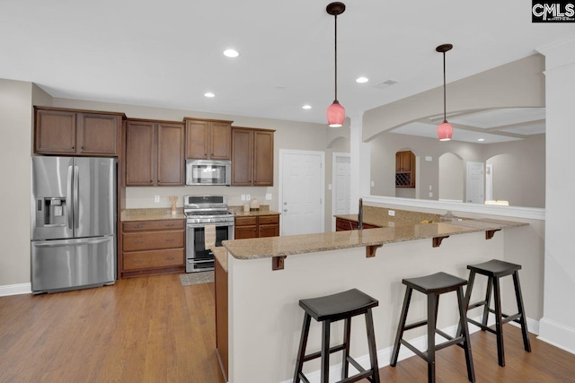 kitchen featuring hanging light fixtures, light wood-type flooring, a kitchen breakfast bar, kitchen peninsula, and stainless steel appliances