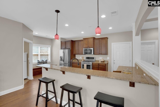 kitchen with light stone counters, hanging light fixtures, light hardwood / wood-style flooring, appliances with stainless steel finishes, and a kitchen breakfast bar