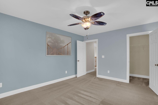 unfurnished bedroom featuring a spacious closet, light colored carpet, a closet, and ceiling fan