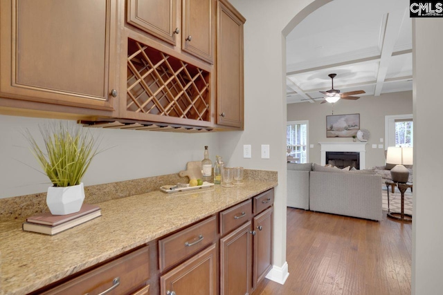 kitchen featuring beamed ceiling, coffered ceiling, ceiling fan, light hardwood / wood-style floors, and light stone countertops