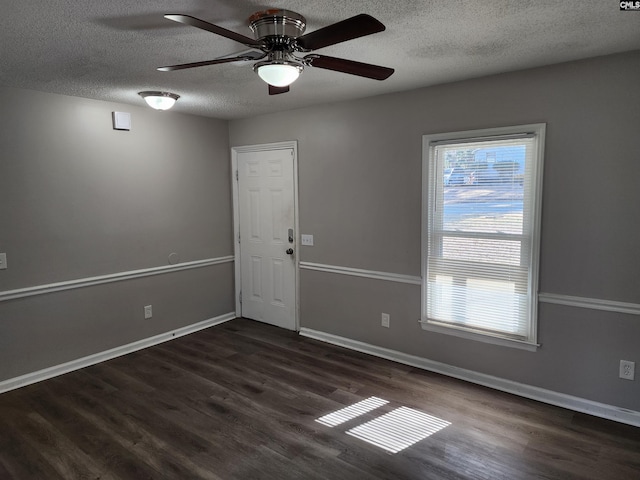 spare room with ceiling fan, dark wood-type flooring, a wealth of natural light, and a textured ceiling