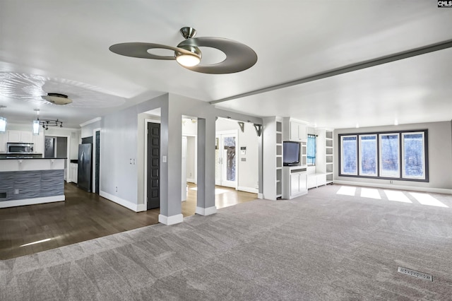 unfurnished living room featuring ceiling fan, rail lighting, dark carpet, and built in shelves